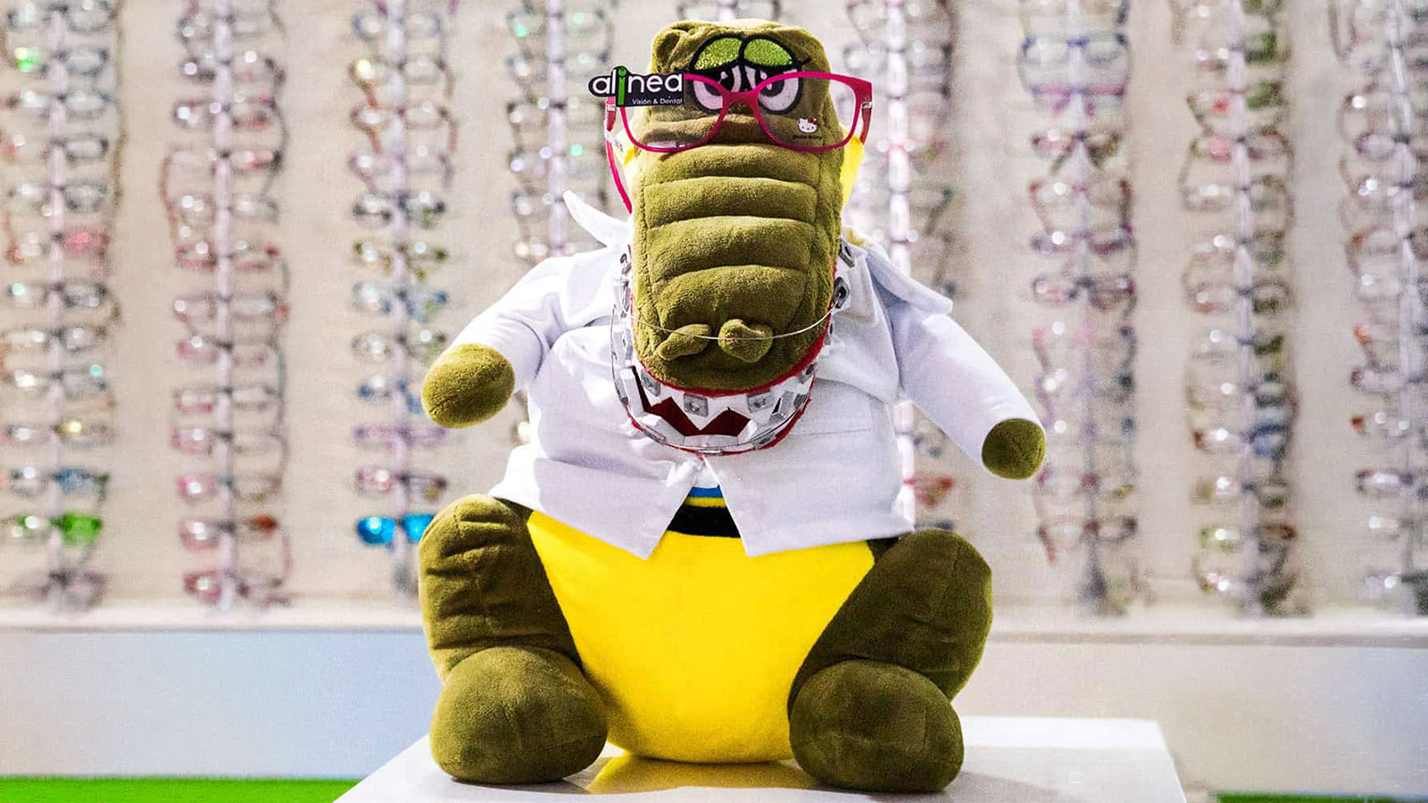 D'Ali, la mascota de Alinea Visión, con bata y lentes en la óptica